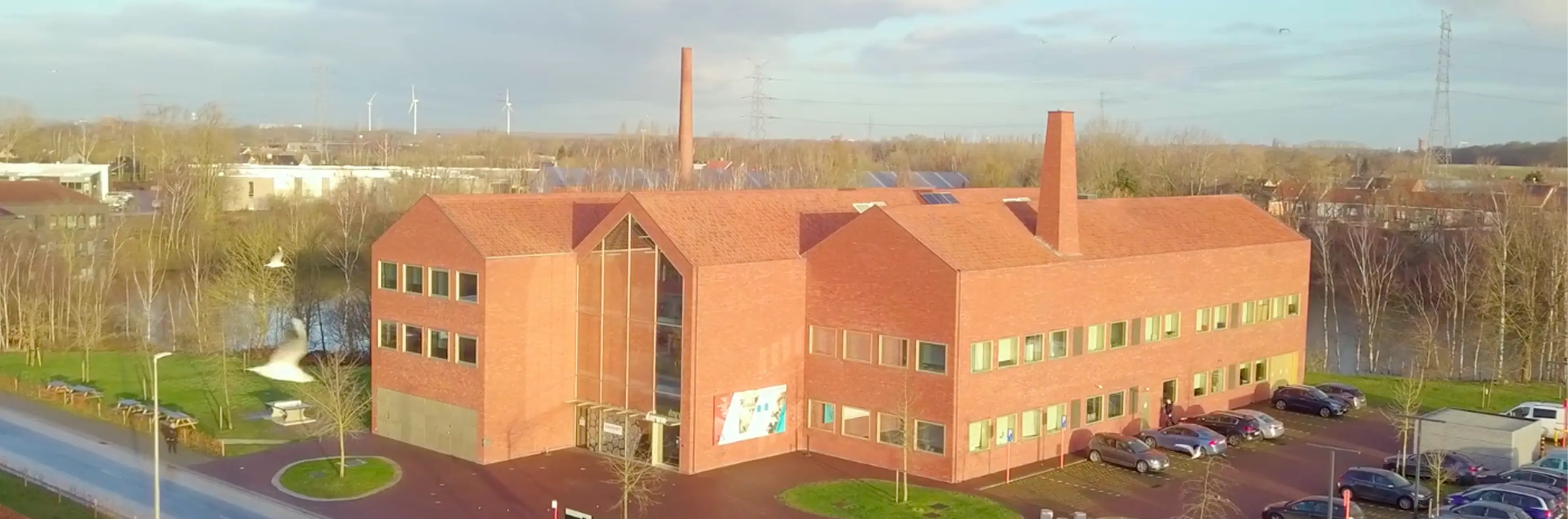 Nowoczesny budynek z czerwonej cegły &ndash; siedziba firmy YUN otoczona zielenią i parkingiem