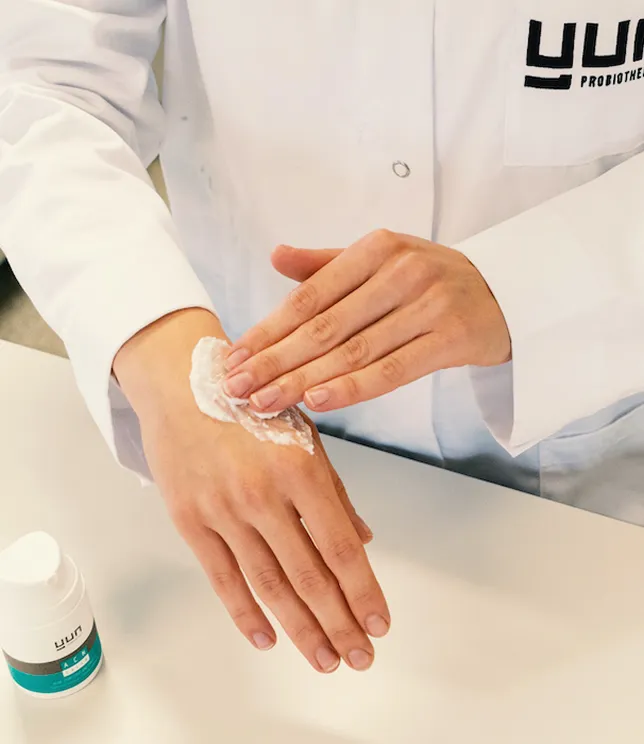 Osoba w białym fartuchu aplikuje krem Yun na dłoń, pokazując spos&oacute;b użycia.